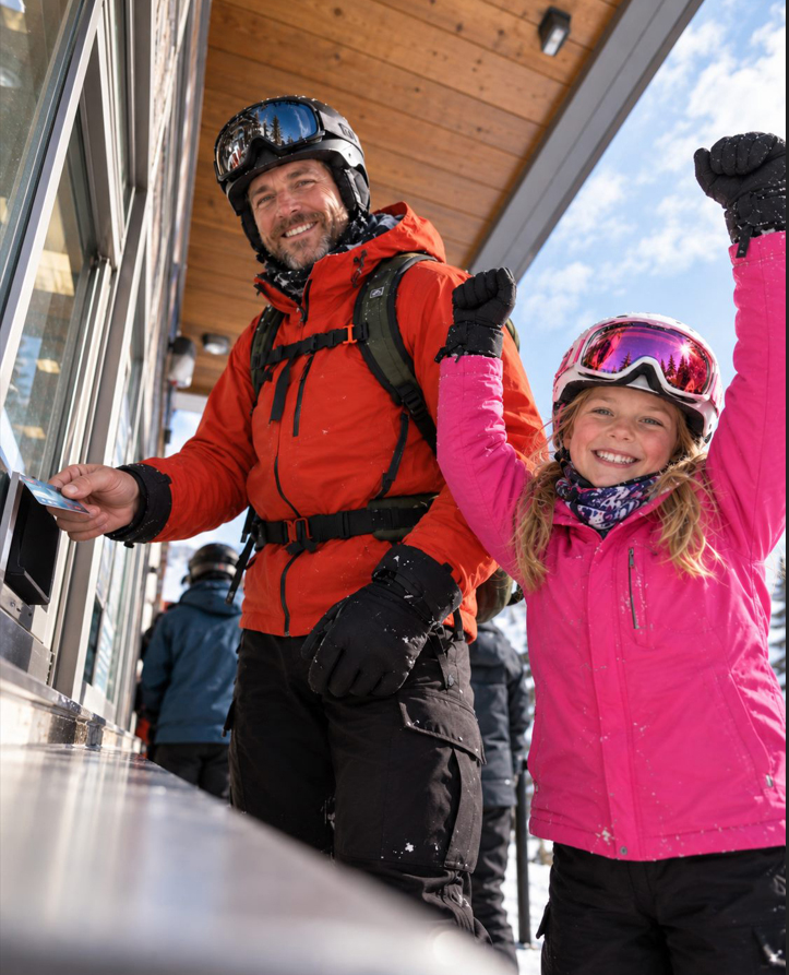 Illustration of an adult and child wearing ski helmets at an outdoor ski ticket window.
