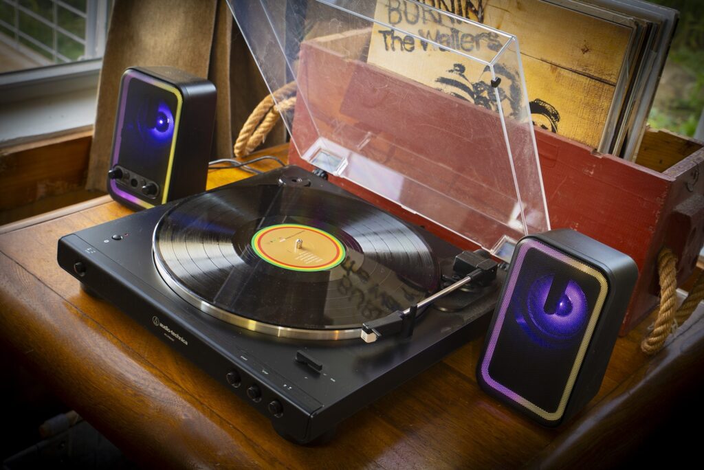 Turntable with a record, two small speakers and a crate of vinyl records on a wooden table