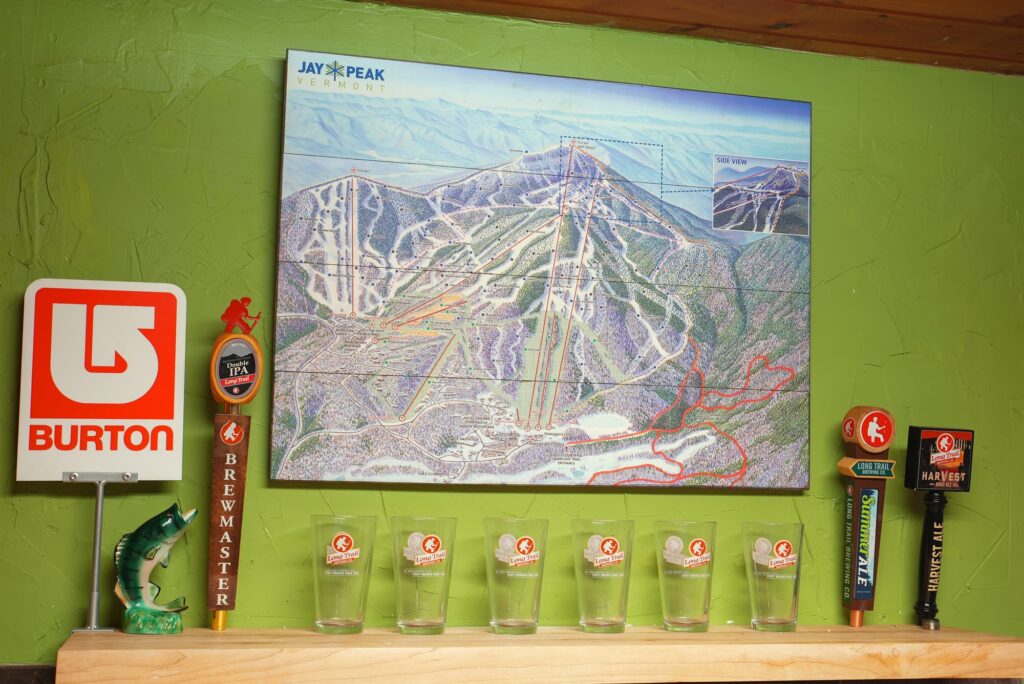 Illustrated Jay Peak trail map on a green wall above a shelf of pint glasses