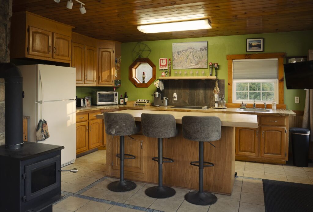 Kitchen with wood cabinets, a butcher-block island with three gray bar stools, and a black wood stove